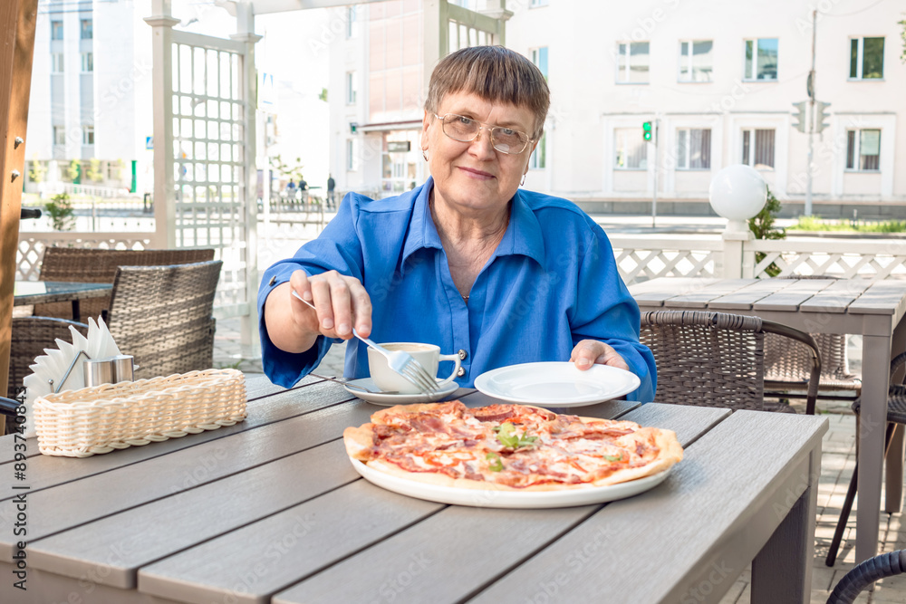 An elderly woman sits in a summer cafe, drinks coffee and pizza. An elderly woman sits in a summer cafe, drinks coffee and pizza.