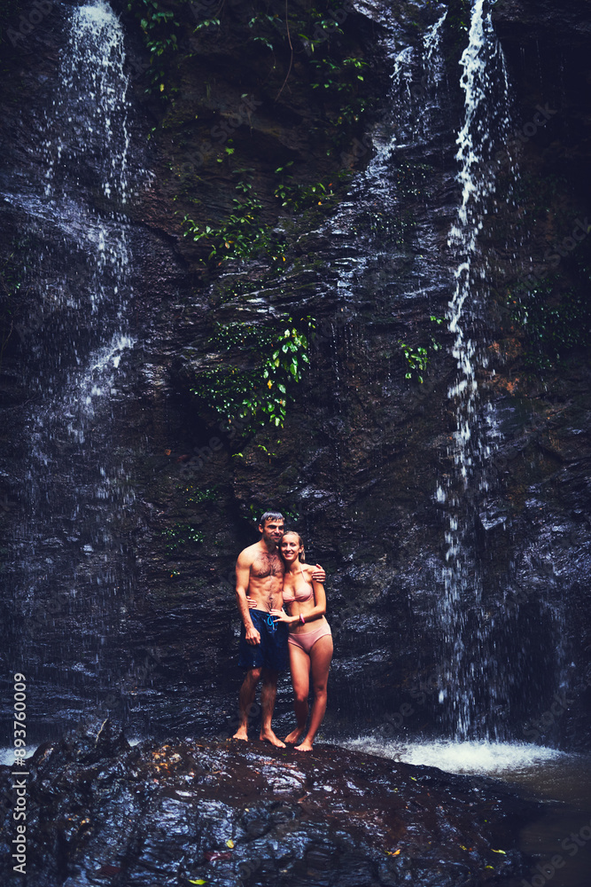 Fototapeta premium Couple, people and happy on waterfall for summer holiday or break to relax, swim and adventure in Thailand. Relationship, nature and smile at river on vacation or journey for bonding with wildlife