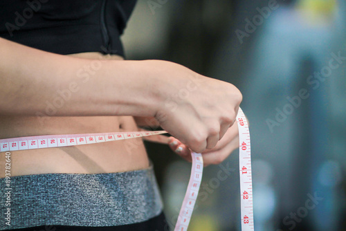 A young woman holds a tape measure to measure her waist circumference after exercising to reduce belly fat and measures her waist circumference to check the results of the weight loss course. photo