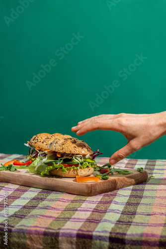 A hand grabbing the tasty fresh sandwich served on the wooden board with a green background
