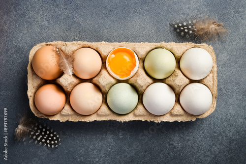 Colored chicken eggs in a paper tray. Food is enriched with proteins. On a stone background. Top view. photo