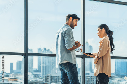 Professional businessman present financial statistic to investor while standing near panoramic window shows skyscraper or city view. Diverse businesspeople discuss about marketing plan. Tracery.