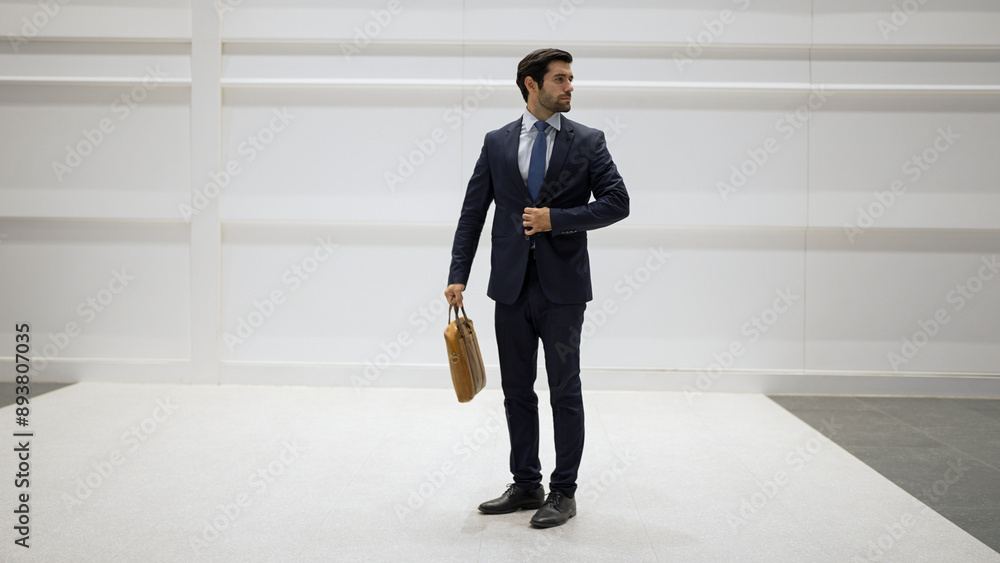 Fototapeta premium Professional business man standing with cool pose at white background. Manager holding bag while finding partner or looking around. Caucasian working man prepare himself for presentation. Exultant.