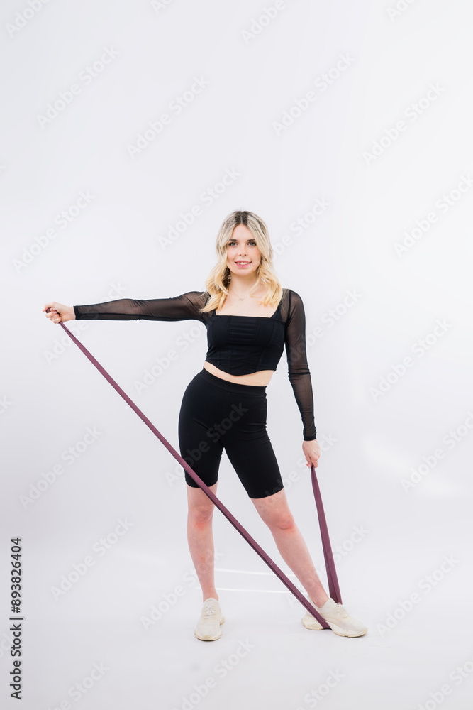 Woman in black sports clothes exercising with resistance band in studio. Woman in black sports clothes exercising with resistance band in studio.