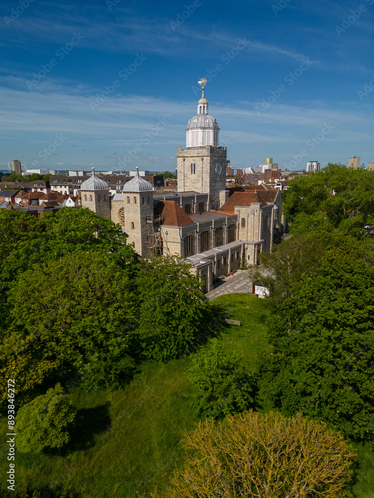 Aerial vertical view of the Portsmouth Cathedral and the city skyline. View towards Gunwharf Quays. Public park with tall green trees. Blue sky on a sunny day.