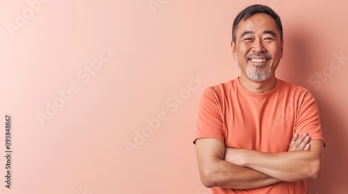 Smiling MiddleAged East Asian Man in Orange Shirt Against Peach Background for Welcoming and Friendly Design