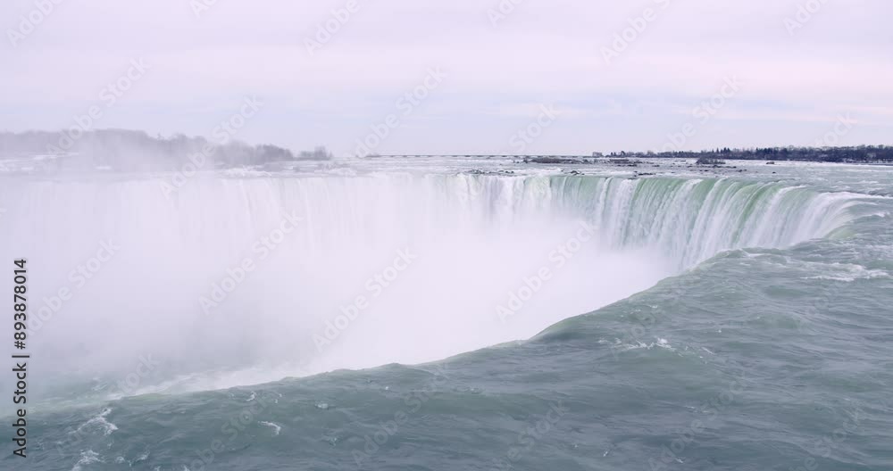 Handheld shot of Niagara Falls with mist rising from the cascading water, surrounded by a winter landscape. Footage shows the top of a large waterfall with water flowing forcefully over the edge Handheld shot of Niagara Falls with mist rising from the cascading water, surrounded by a winter landscape. Footage shows the top of a large waterfall with water flowing forcefully over the edge