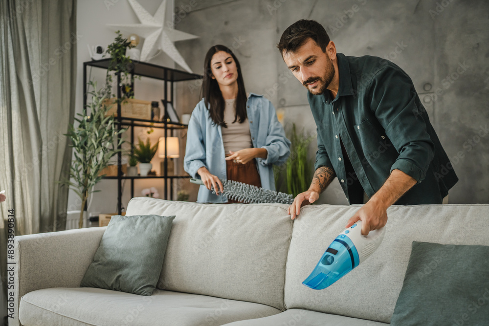 adult man vacuum sofa with hand vacuum cleaner while woman support him adult man vacuum sofa with hand vacuum cleaner while woman support him