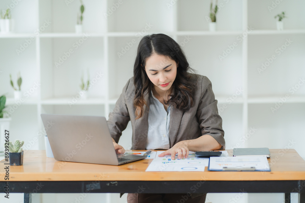 Focused on Success: A young businesswoman meticulously analyzes financial data, her brow furrowed in concentration as she works diligently on her laptop. Her dedication and focus portray the drive and