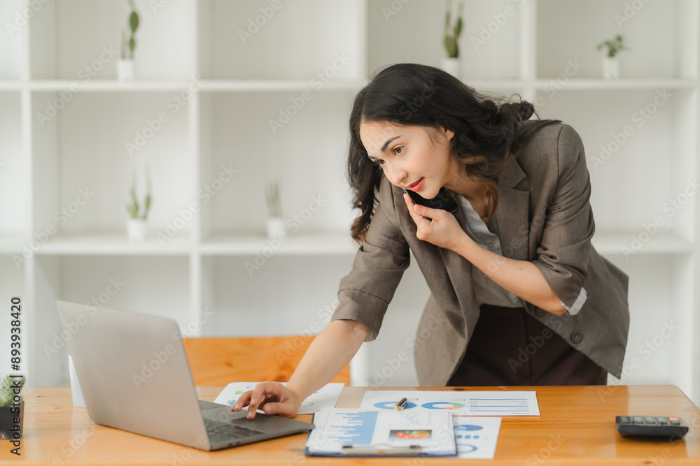 Beautiful businesswoman using laptop and talking on the phone in the office Beautiful businesswoman using laptop and talking on the phone in the office