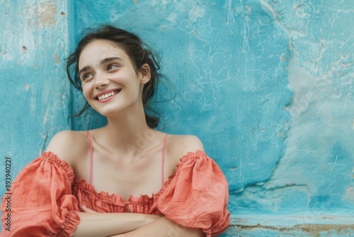A woman in a stunning red dress leans against a vibrant blue wall, exuding grace and poise