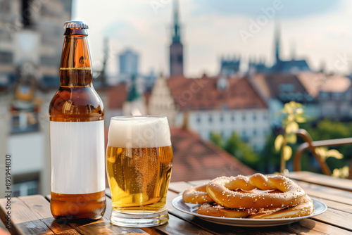 A close up of a bottle of beer with a blank mock up label on it and a glass of beer served together with brezels on the wooden table with a city skyline in the background photo