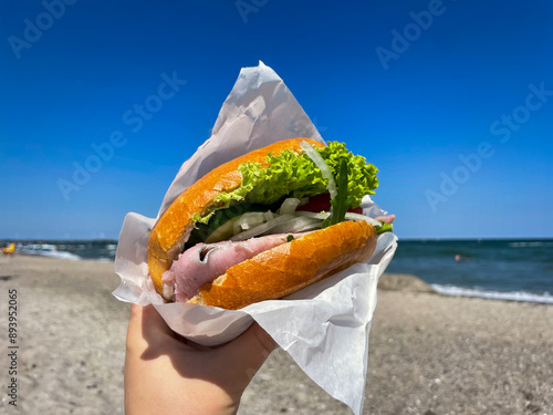 Traditional north germany snack street food Fischbroetchen matjes fish fillet with onion and salad leaves in a wheat bun in female hand close up on Baltic sea beach  photo