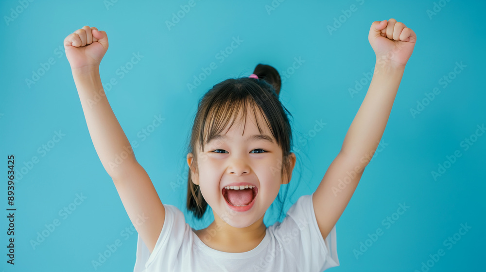Excited little girl with pigtails raising her arms in joy, wearing yellow shirt, smiling broadly against a bright blue background Excited little girl with pigtails raising her arms in joy, wearing yellow shirt, smiling broadly against a bright blue background