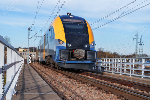 Modern train on electrified railway tracks. Overhead power lines and white safety barriers are visible. Rail infrastructure showcasing public transport and green travel technologies photo