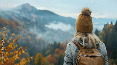 A woman wearing a brown hat and a backpack is standing on a mountain top