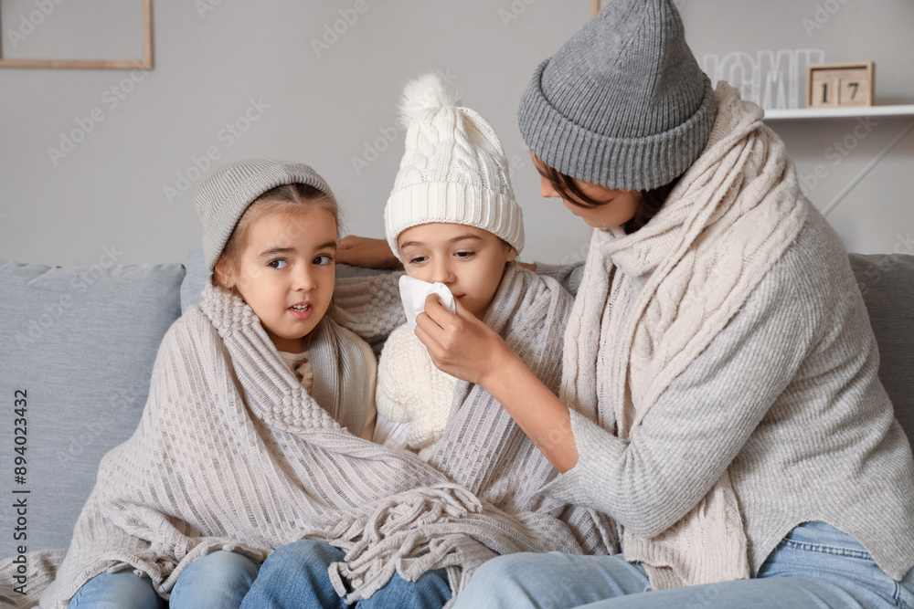 Mother with her ill little daughters sitting on sofa at home Mother with her ill little daughters sitting on sofa at home