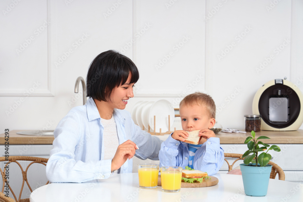 Young mother with her little son having breakfast at table in kitchen Young mother with her little son having breakfast at table in kitchen