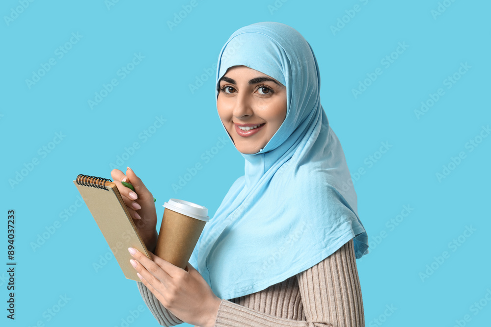 Beautiful Muslim woman with notebook and cup of coffee on color background Beautiful Muslim woman with notebook and cup of coffee on color background