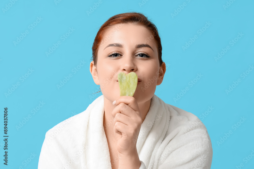Beautiful young woman covering mouth with guasha tool on blue background, closeup Beautiful young woman covering mouth with guasha tool on blue background, closeup