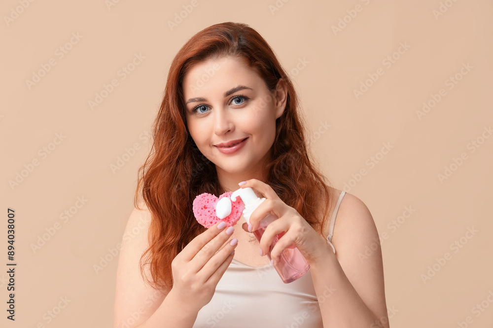 Beautiful young woman with cosmetic product and heart-shaped bath sponge on beige background Beautiful young woman with cosmetic product and heart-shaped bath sponge on beige background