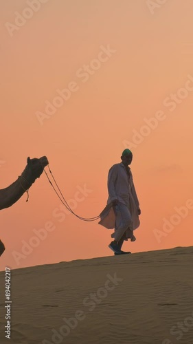 Indian cameleers (camel driver) bedouin with camel silhouettes in sand dunes of Thar desert on sunset. Caravan in Rajasthan travel tourism background safari adventure. Jaisalmer, Rajasthan, India