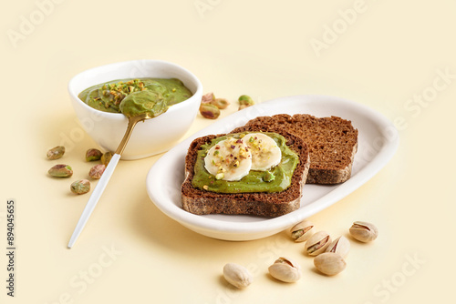 Bowl and pieces of bread with tasty pistachio paste on yellow background