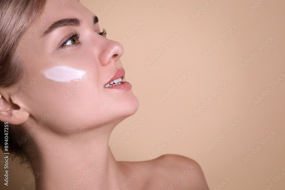 Fototapeta premium Beautiful woman with cream on her face against beige background, closeup. Space for text