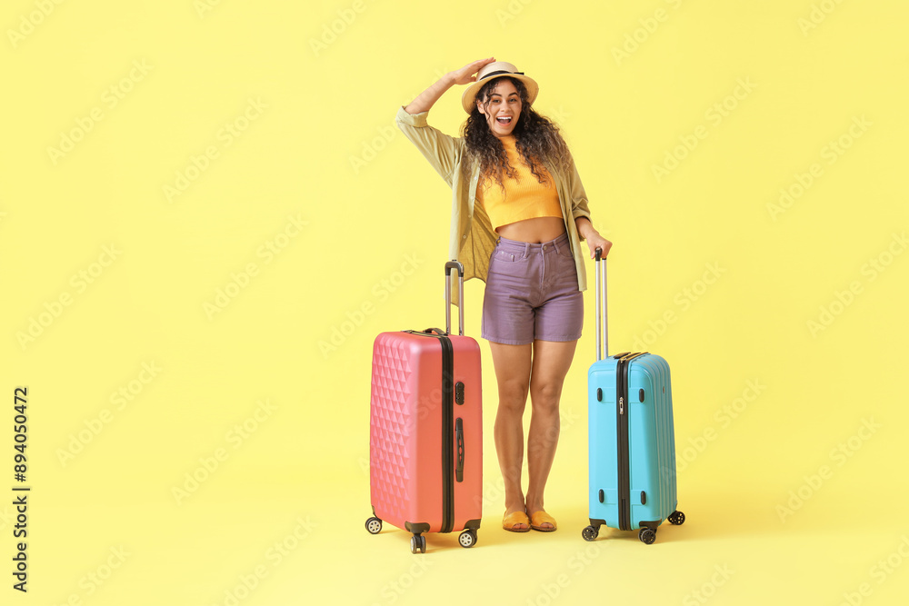 Young African-American woman with suitcases on yellow background Young African-American woman with suitcases on yellow background