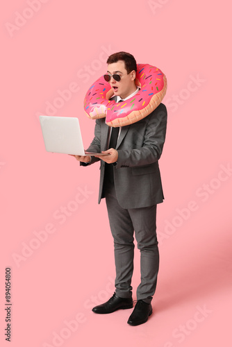 Office worker with laptop and inflatable ring dreaming about vacation on pink background