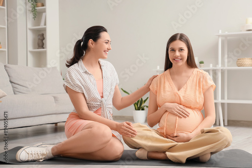 Young pregnant woman with doula sitting on mat at home