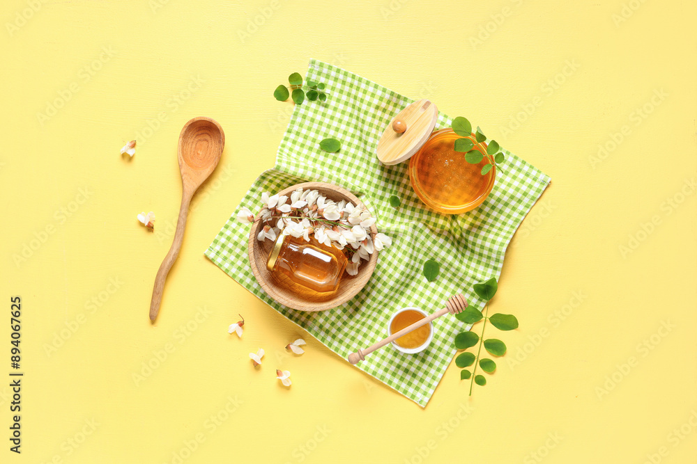 Jars and bowl of sweet honey with acacia flowers on yellow background Jars and bowl of sweet honey with acacia flowers on yellow background