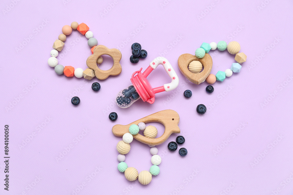Composition with baby nibbler, blueberry and wooden teethers on lilac background Composition with baby nibbler, blueberry and wooden teethers on lilac background