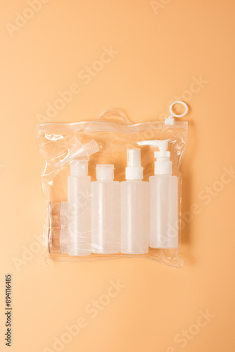 Plastic bag with cosmetic travel kit on beige background. A set of travel-size hand luggage beauty travel kit for the face, body and hair in a clear plastic bag