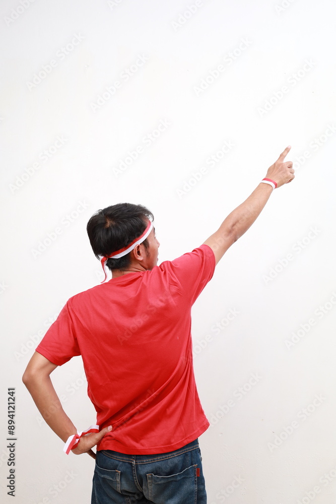 Naklejka premium Back view of Young asian boy with red white ribbon celebrating Indonesia independence day while pointing above