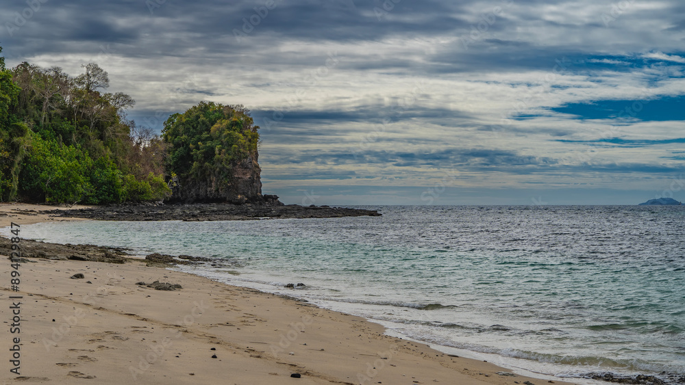 Secluded beach on a tropical island. Footprints on the sand. Ripples on the turquoise ocean. A picturesque rock on a background of blue sky and clouds. Madagascar. Nosy Tanikely Secluded beach on a tropical island. Footprints on the sand. Ripples on the turquoise ocean. A picturesque rock on a background of blue sky and clouds. Madagascar. Nosy Tanikely