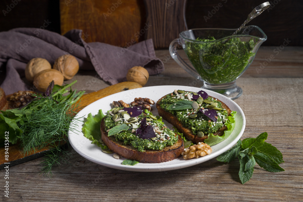 Toasts with homemade pesto sauce with sunflower seeds, sesame seeds and basil leaves on a light plate Toasts with homemade pesto sauce with sunflower seeds, sesame seeds and basil leaves on a light plate