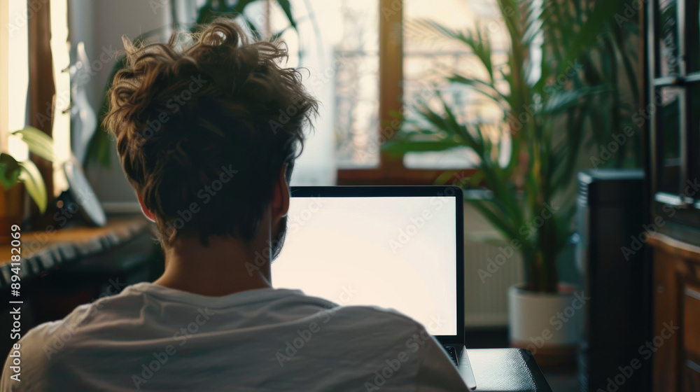 Over-the-shoulder shot of a young man working on a laptop with a blank white screen at home Over-the-shoulder shot of a young man working on a laptop with a blank white screen at home