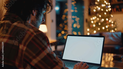 Over-the-shoulder view of a young man typing on a laptop with a white blank screen at home