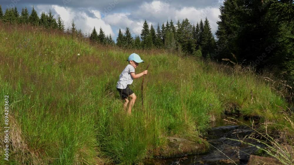 Lonely boy walks near a stream with a stick in his hands on a sunny day. Child safety at a body of water. High quality 4k footage Lonely boy walks near a stream with a stick in his hands on a sunny day. Child safety at a body of water. High quality 4k footage