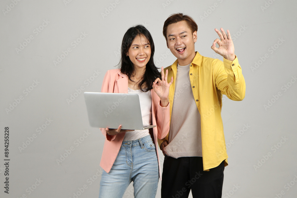 portrait of happy asian Indonesian couple holding laptop computer and giving ok sing finger gesture on isolated background portrait of happy asian Indonesian couple holding laptop computer and giving ok sing finger gesture on isolated background