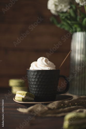 a cup of whipped cream sits on a table next to a vase with flowers.