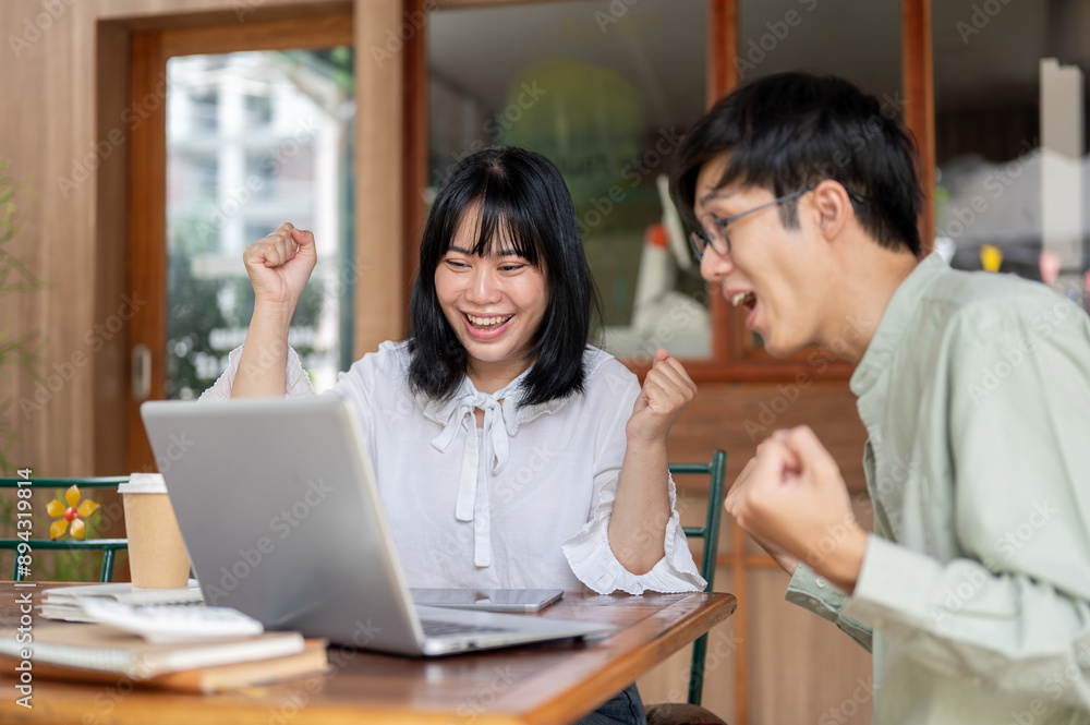 Two cheerful Asian friends, male and female, are sitting at a cafe, celebrating good news together. Two cheerful Asian friends, male and female, are sitting at a cafe, celebrating good news together.