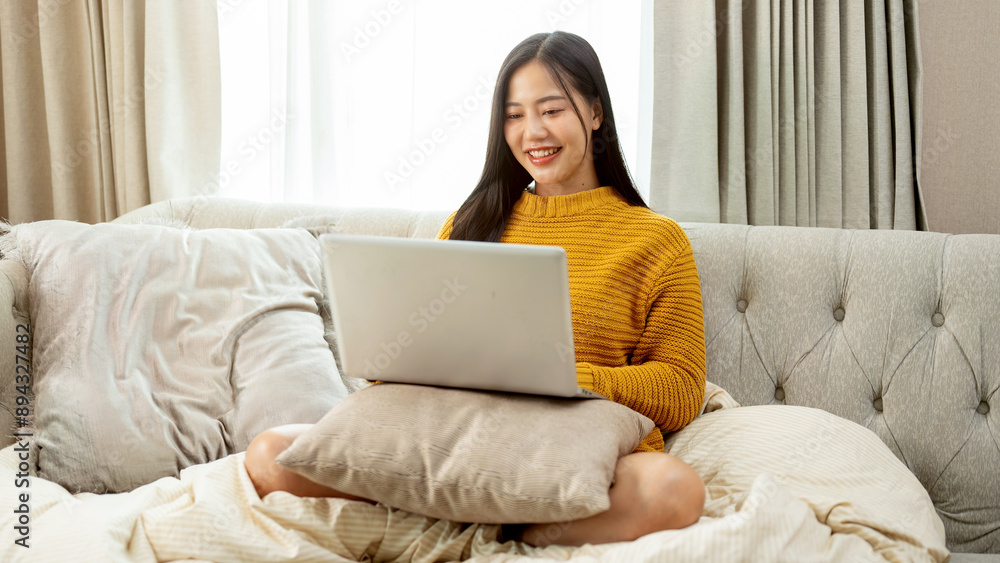 An attractive Asian woman in comfy clothes is using a laptop computer on a couch at home. An attractive Asian woman in comfy clothes is using a laptop computer on a couch at home.