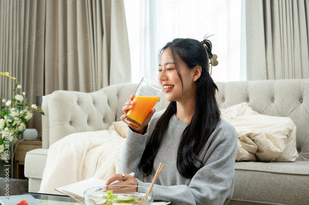An attractive Asian woman is drinking orange juice at a coffee table in the living room. An attractive Asian woman is drinking orange juice at a coffee table in the living room.