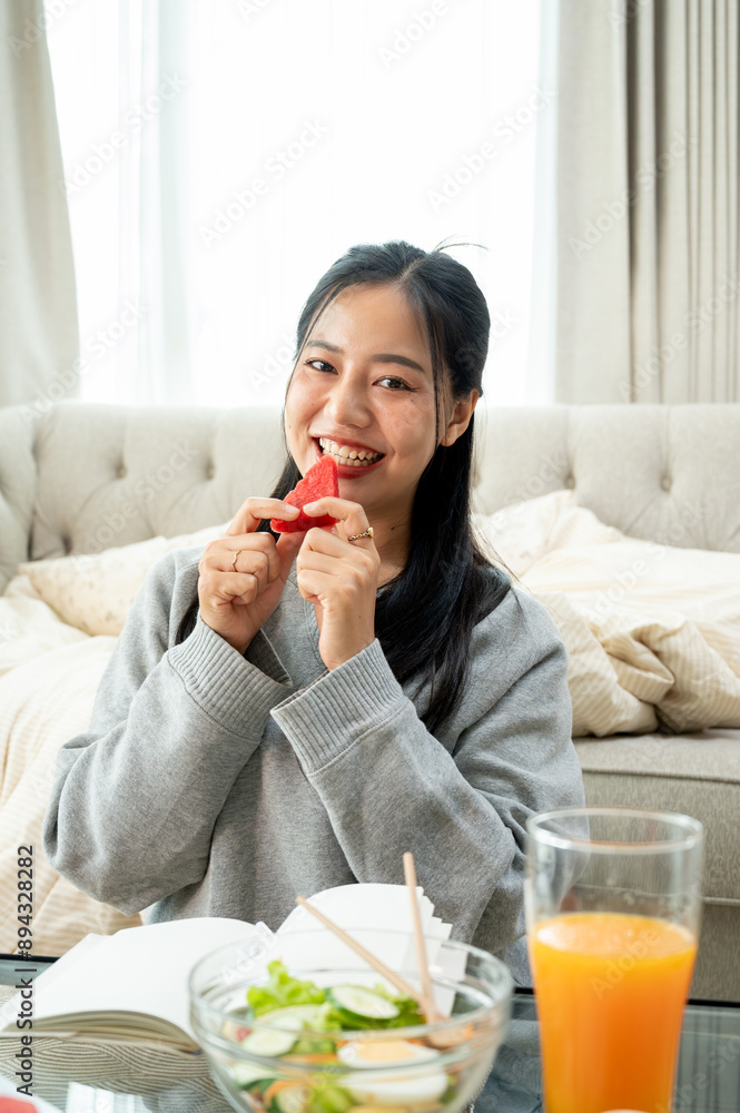 A beautiful Asian woman is posing with a piece of watermelon, sitting at a coffee table. A beautiful Asian woman is posing with a piece of watermelon, sitting at a coffee table.