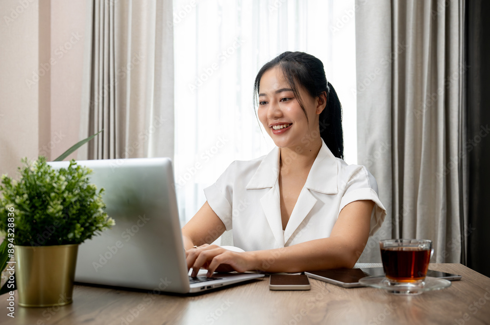 A charming Asian businesswoman is working on her laptop computer at her desk in the office. A charming Asian businesswoman is working on her laptop computer at her desk in the office.