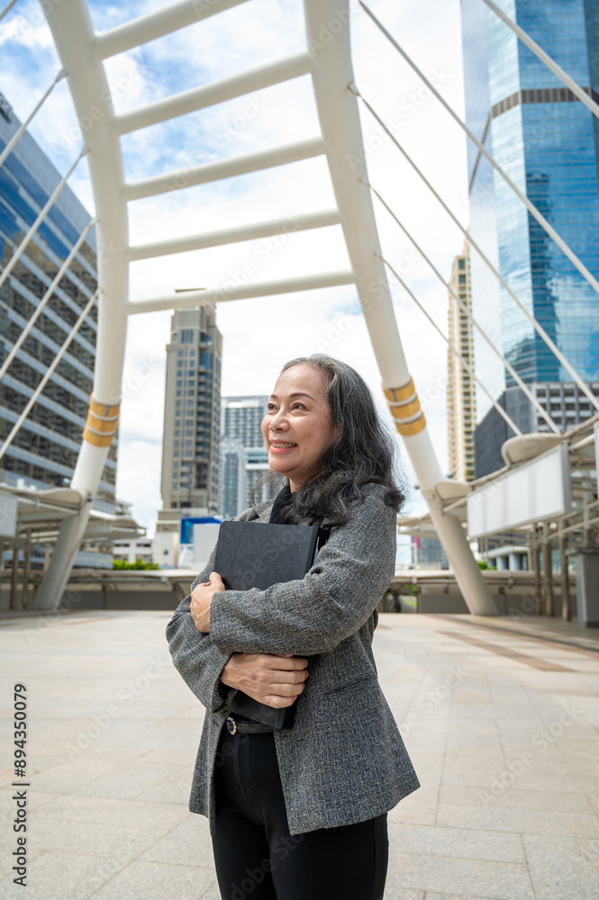 A successful mature Asian businesswoman in a suit is looking away at the sky, standing in the city. A successful mature Asian businesswoman in a suit is looking away at the sky, standing in the city.