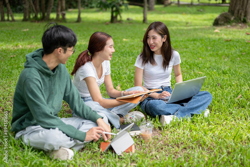A group of cheerful Asian students sits and talks in the green park, enjoying their conversation.