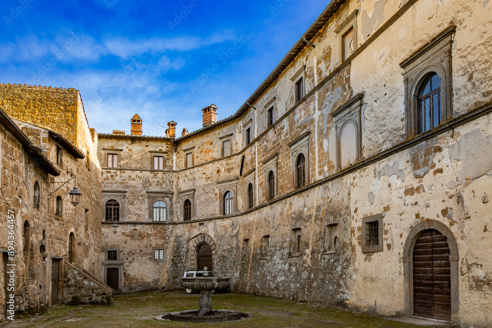 A glimpse of the ancient medieval village of Montecalvello, Viterbo, Italy. The internal courtyard of the castle with the ancient stone and brick buildings and the fountain in the center. A glimpse of the ancient medieval village of Montecalvello, Viterbo, Italy. The internal courtyard of the castle with the ancient stone and brick buildings and the fountain in the center.
